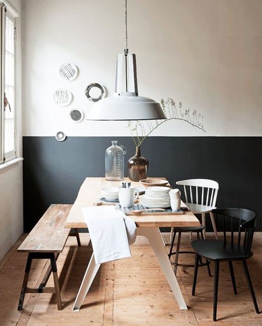 a catchy modern dining room with a color block wall, a stained table, a bench and black and white chairs, a gallery wall of plates