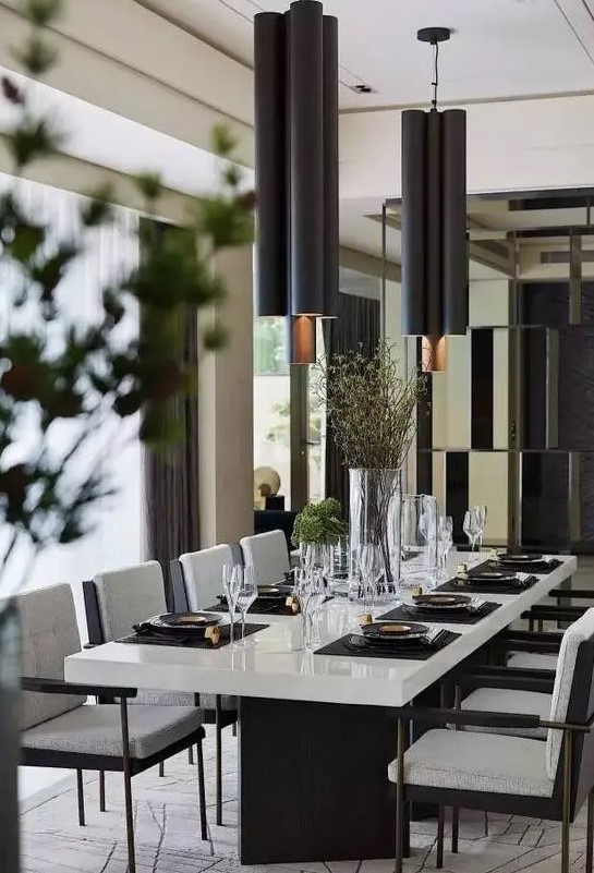 a chic contemporary dining space with a white table with black legs, black chairs with white upholstery, black pendant lamps and greenery