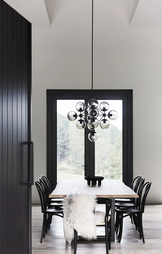 a chic dining room wiht a living edge dining table, black chairs, faux fur and a bubble chandelier with smoked glass