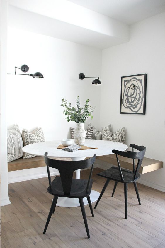 a cozy farmhouse dining nook with a floating bench, a round table, black chairs, black sconces and an artwork