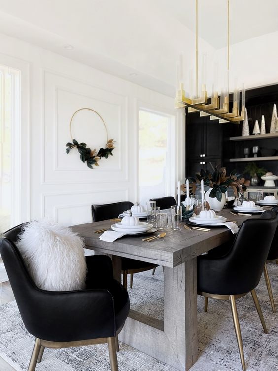 a glam dining room with a black accent wall and built-in cabinets, a stained table and black chairs, a gold chandelier