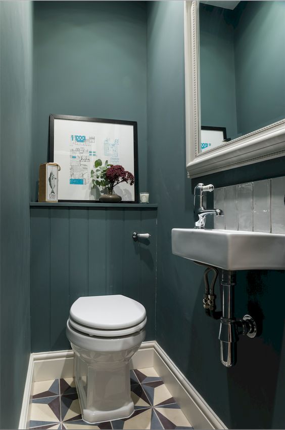 a guest toilet done with teal walls, a large mirror in a frame, some artworks and a wall mounted sink a guest toilet done with teal walls, a large mirror in a frame, some artworks and a wall-mounted sink