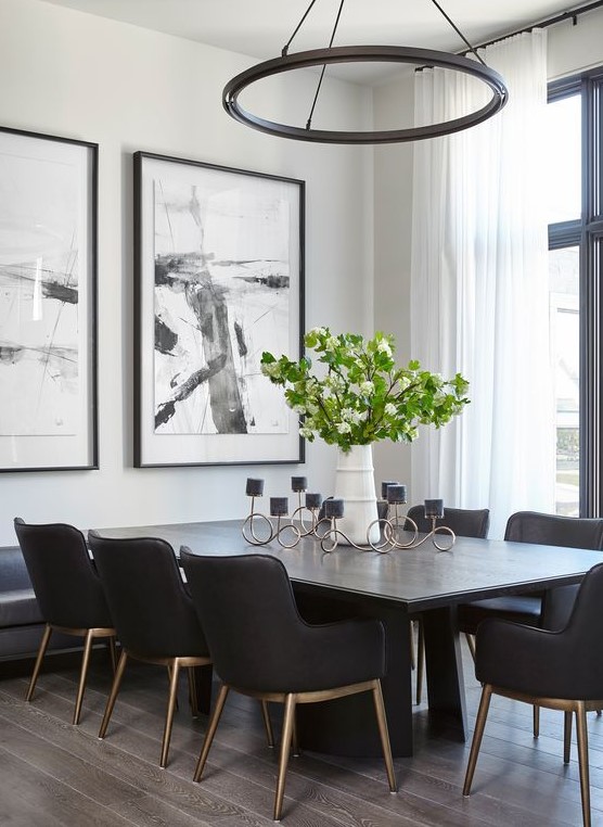 a light-filled black and white dining room with white walls, a black table and chairs, a round chandelier and catchy artwork