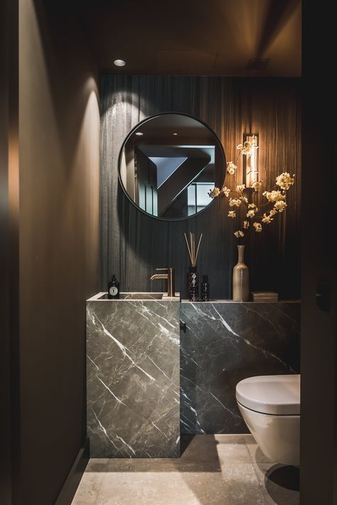 a luxurious contemporary guest toilet with a stone sink and vanity, a mirror and soem stone on the wall plus blooms