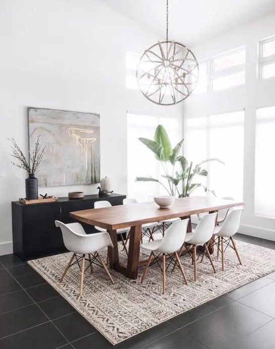 a mid-century modern dining space with a stained table and white Eames chairs, a printed rug, a black credenza, a sphere chandelier and potted plants