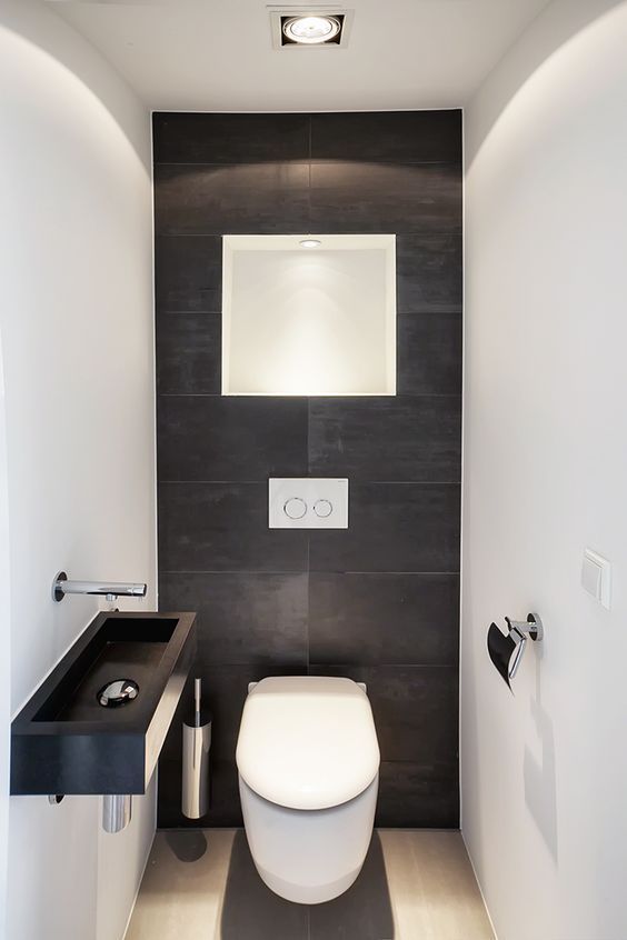 a minimalist guest bathroom with black and white tiles of different sizes, a black wall-mounted sink and some lights