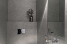 a minimalist guest toilet done with concrete, a wall-mounted sink, a lamp and a large mirror