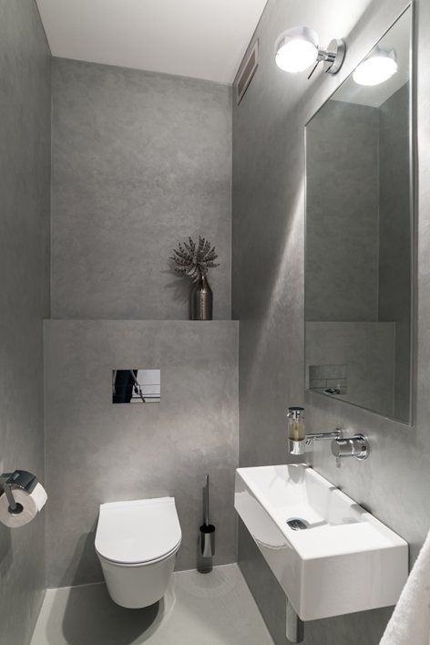 a minimalist guest toilet done with concrete, a wall mounted sink, a lamp and a large mirror