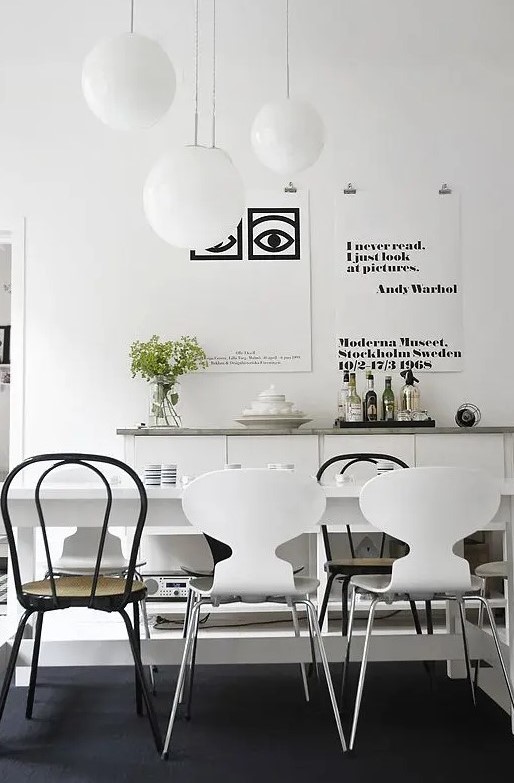 a modern Scandinavian dining room with a white table, mismatching black and white chairs, a sleek white credenza with a wooden countertop and a black and white gallery wall