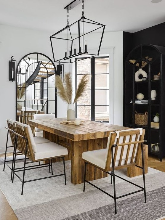 a modern boho dining room with a black accent wall and a storage unit, a stained table, neutral chairs, a black chandelier