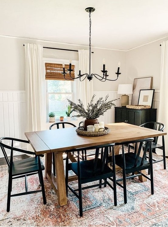 a modern farmhouse dining space with a stained table, black chairs, a black cabinet, a vintage chandelier and a printed rug