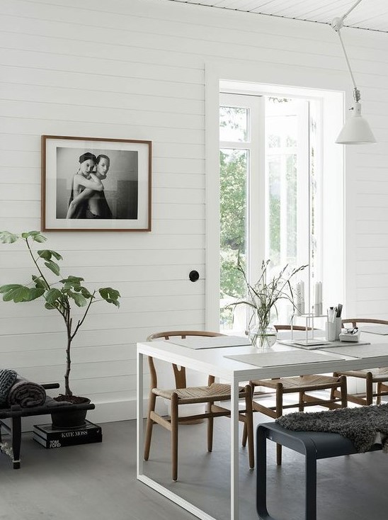 a monochromatic Scandinavian dining room with a white dining table, black and stained chairs, potted greenery and artwork