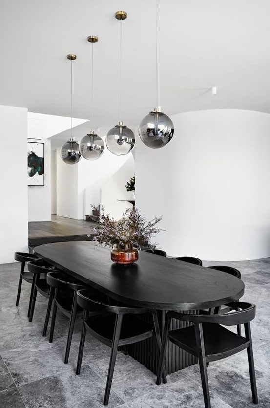 a monochromatic dining room with an oval table and black chairs, smoked glass pendant lamps and white curved walls