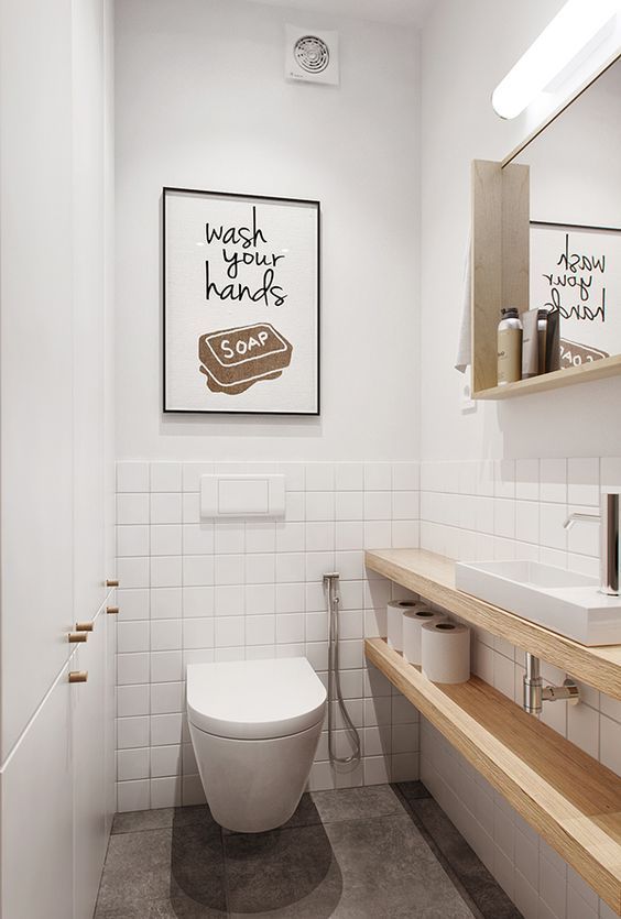 a simple and cntemporayr guest toilet with white and white tile walls, a mirror in a wooden frame, wooden shelves for storage and a sign