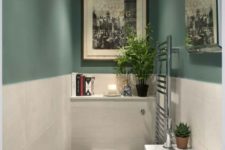a small and stylish guest toilet with green and white tile walls, a sink with a vanity for storage and some artworks