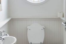 a small nautical guest toilet with paneling, a round window with a boat, a wall-mounted sink