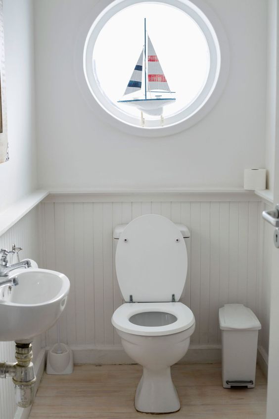 a small nautical guest toilet with paneling, a round window with a boat, a wall mounted sink