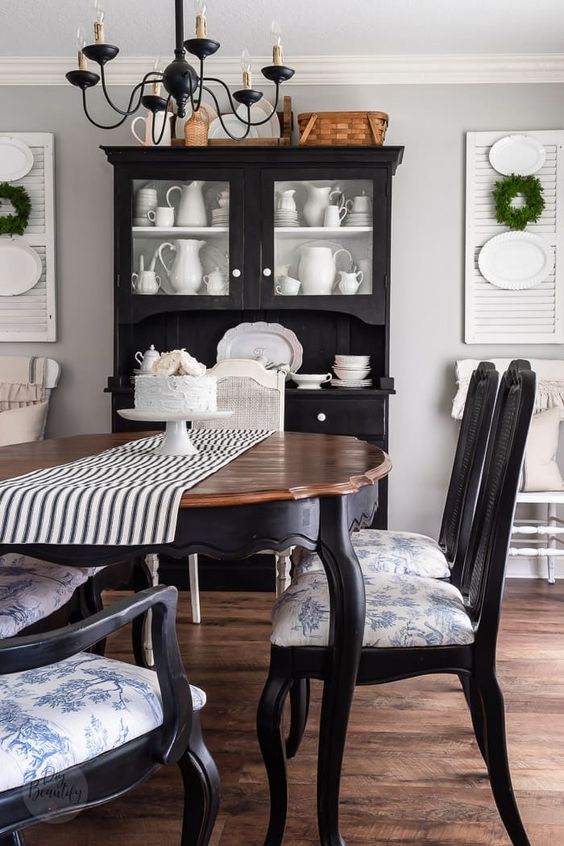 a vintage farmhouse dining room with a black buffet, a vintage table, black chairs with blue upholstery, a black chandelier