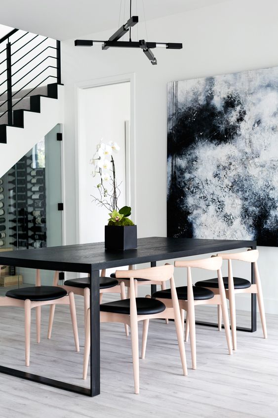 an edgy dining space with a black dining table, stained wood and black chairs, a bold artwork and a catchy chandelier