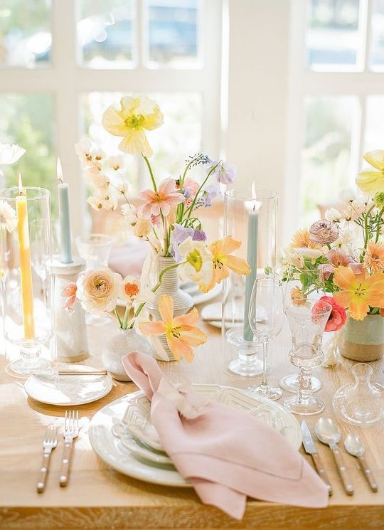 a beautiful pastel Mother's Day tablescape with yellow, pink, lilac and orange blooms, neutral porcelain, pastel candles and pink napkins