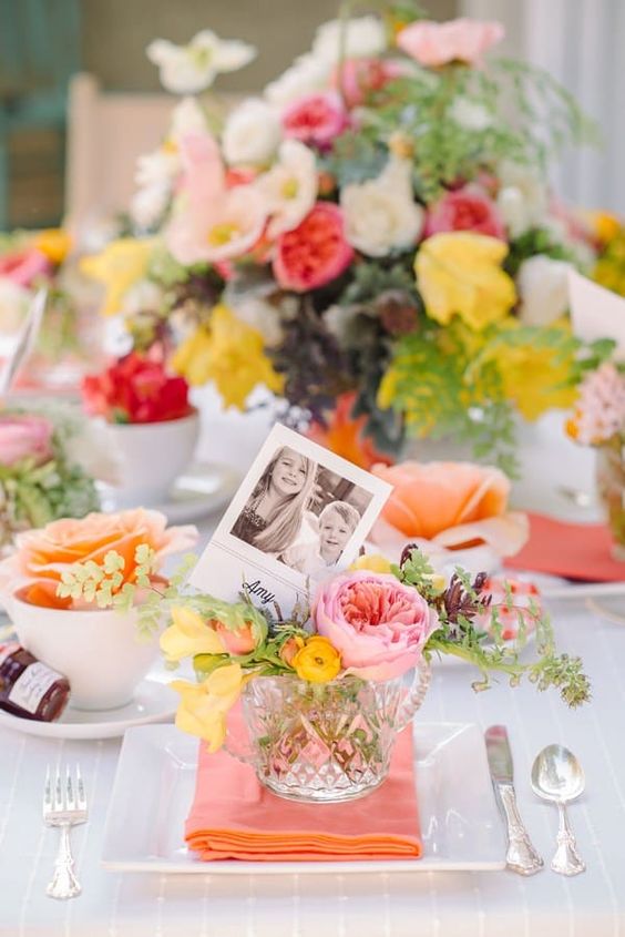 a bright Mother's Day tablescape with bold blooms and greenery, coral napkins and photos plus silver cutlery