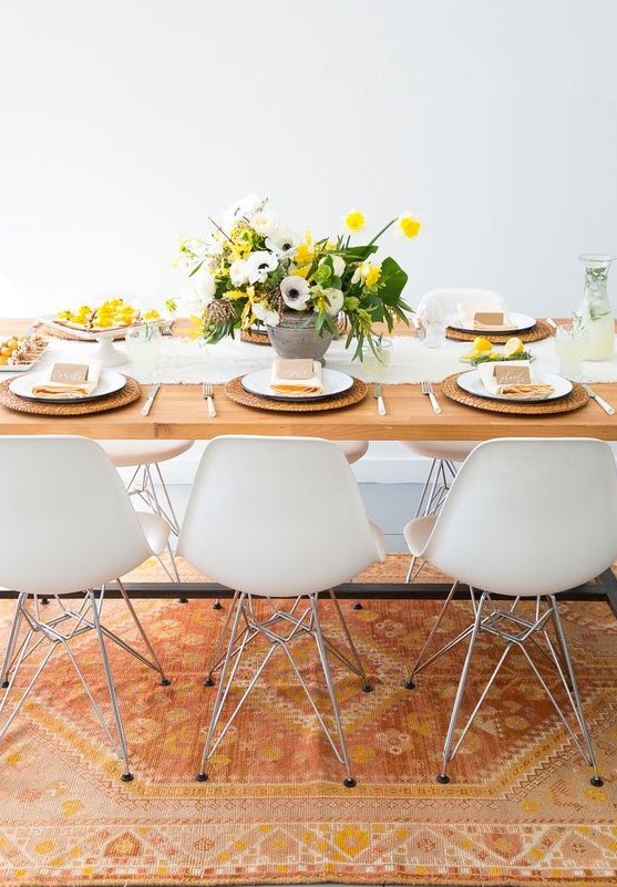 a bright and fresh spring table setting with a yellow and spring floral centerpiece, wicker chargers, a white runner and yellow napkins