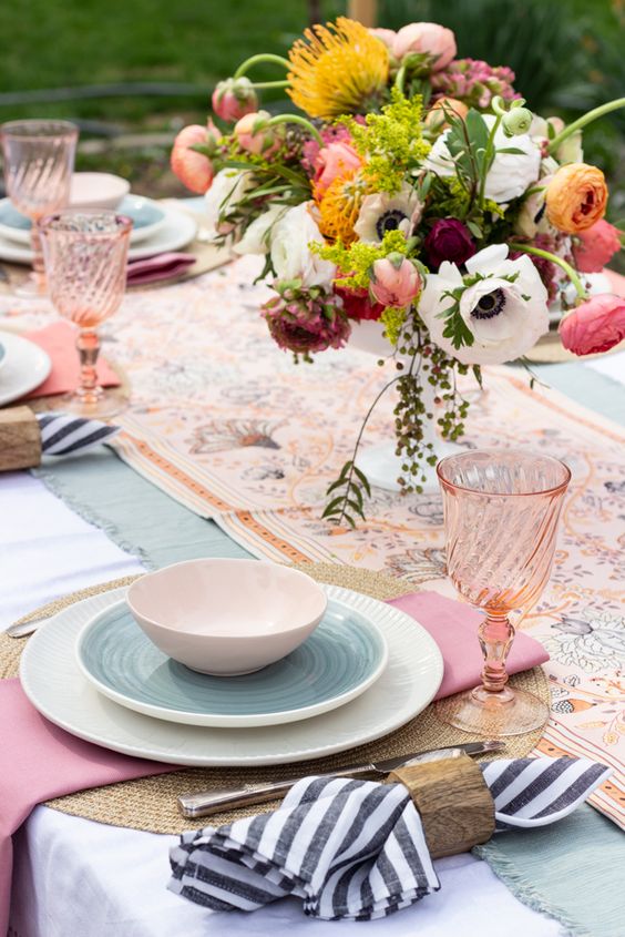 a colorful Mother's Day table setting with printed napkins and runner, bold blooms and greenery, wicker placemats, pink glasses