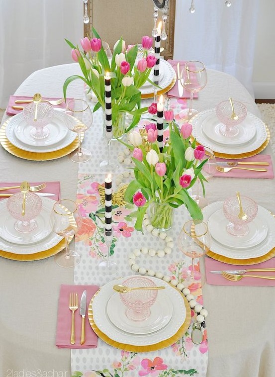 a colorful spring table setting with pink napkins, a floral table runner, wooden beads and striped candles plus pink glass