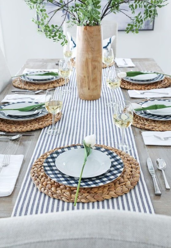 a fresh modern spring table setting with a striped table runner, checked plates, wicker chargers, greenery and white tulips