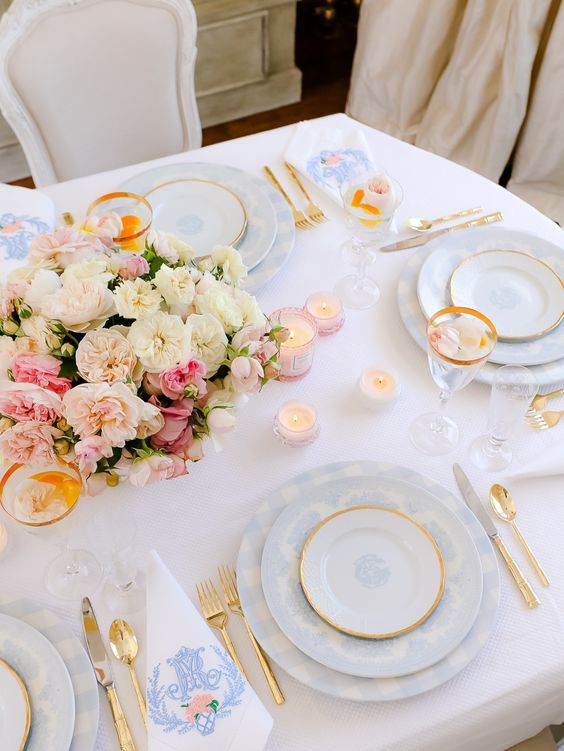 a lovely Mother's Day tablescape with blue plates and gold cutlery, a lovely blush and white floral centerpiece and candles