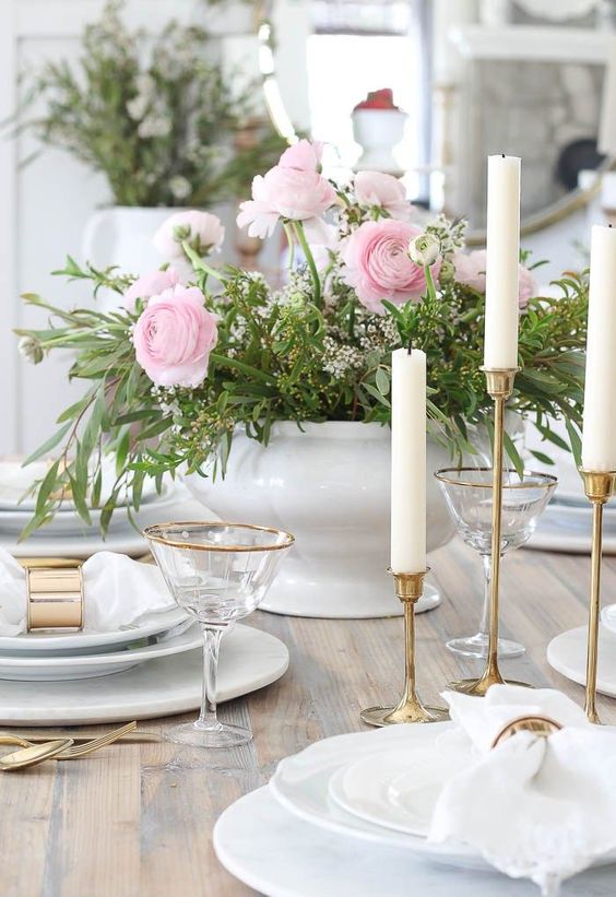 a refined Mother's Day tablescape with pink and white blooms and greenery, white plates and napkins, tall and thin candles