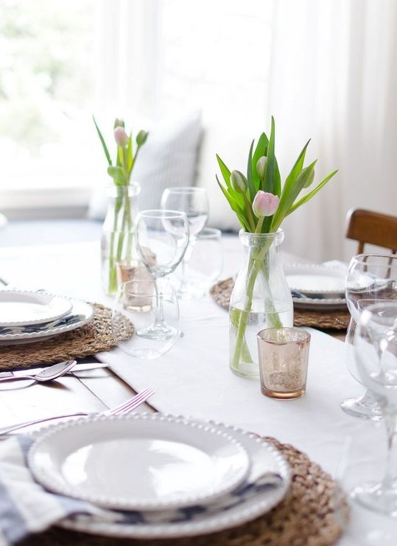 a simple and modern Mother's Day tablescape with a white table runner, tulip centerpieces, wicker chargers and white porcelain