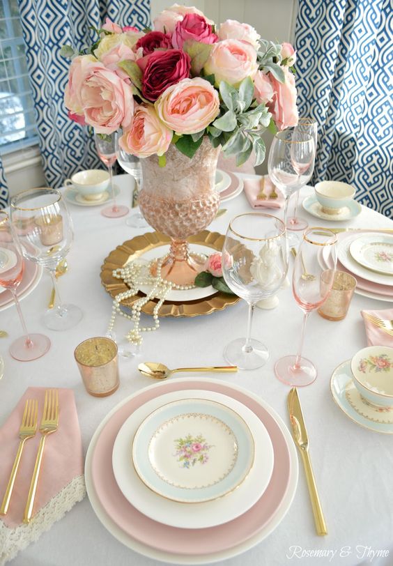 a vintage Mother's Day tablescape with pink and blue plates, pink glasses and napkins and a pink floral centerpiece with pearls