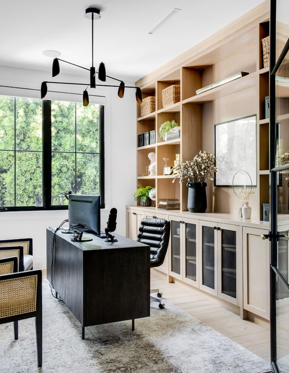 a beautiful and contrasting home office with light-stained cabinetry, a black desk and a chair, cane chairs and a black chandelier