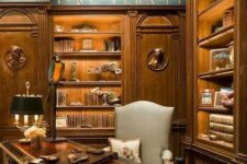 a breathtaking vintage home office with printed wallpaper, stained built-in shelves, a gorgeous dark-stained desk and a grey chair