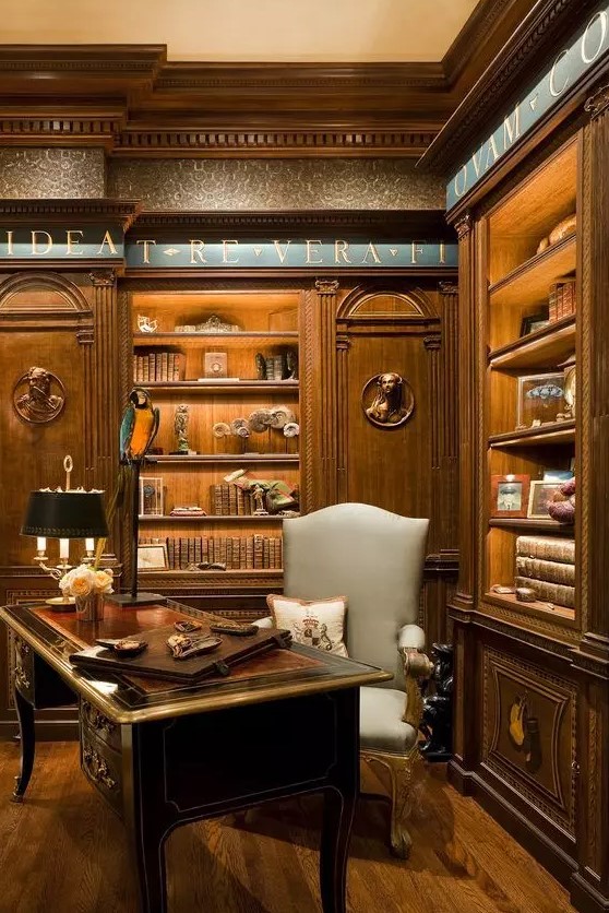 a breathtaking vintage home office with printed wallpaper, stained built-in shelves, a gorgeous dark-stained desk and a grey chair