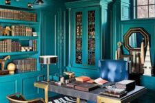 a bright maximalist home office with teal walls and matching built-in furniture and shelves, a refined desk, a navy and leather chairs, a chic chandelier