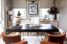 a catchy and chic taupe home office with a light-stained console, a black desk, rust-colored chairs and a chic chandelier