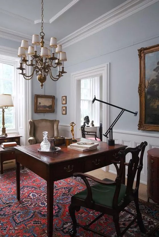 a chic vintage home office with a rich-stained desk, a green chair and a taupe one, a chic chandelier and a printed rug