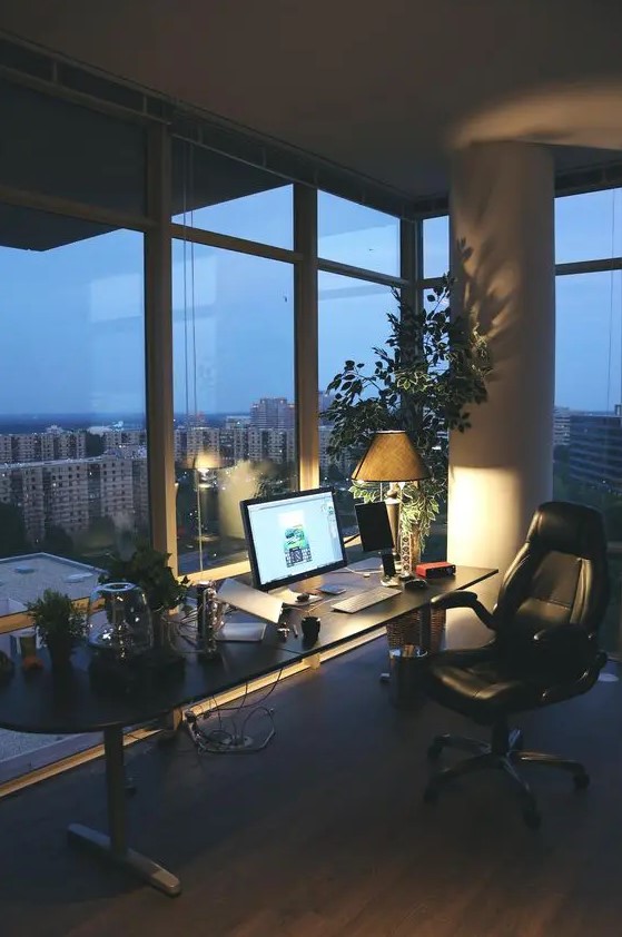 a contemporary home office with glazed wall, a black desk and a black leather chair, potted greenery and a tree and lights