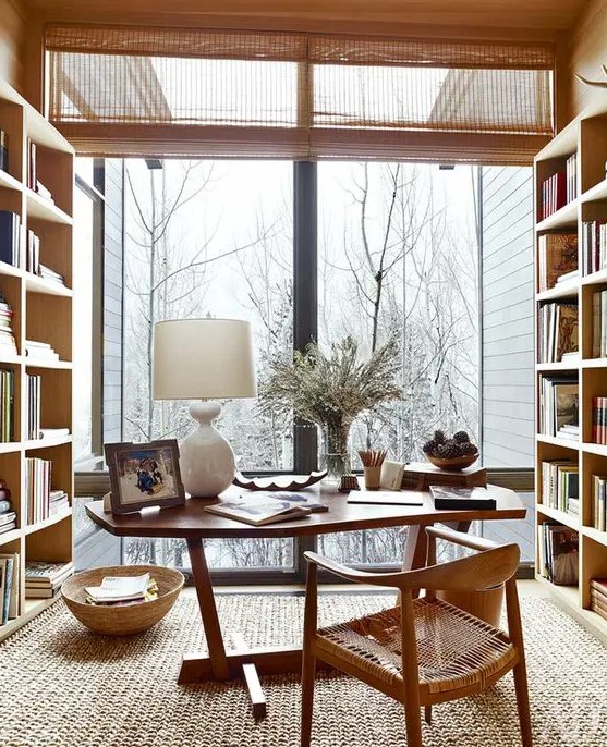 a gorgeous modern country home office with shelving units, a desk, a woven chair, a glazed wall for a lovely view and some wooden accessories