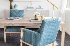 a gorgeous seaside home office with a wooden desk, blue chairs, a sea-inspired artwork, an elegant and catchy table lamp