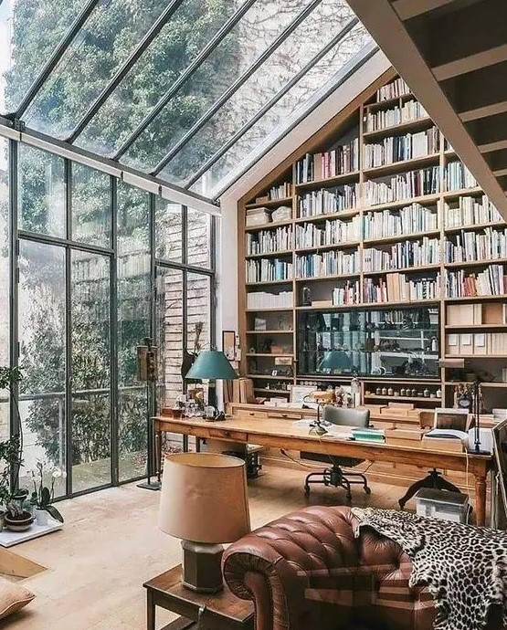 a greenhouse-style home office with an oversized bookcase reaching the roof, a glazed wall and ceiling with garden views and cool vintage and modern furniture