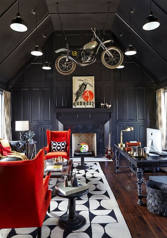 a jaw-dropping black attic home office with a vintage desk, a sitting zone with a black sofa and red chairs, a fireplace and a motorcycle