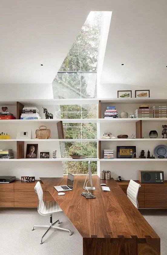 a jaw-dropping contemporary home office with a window skylight, open shelves with books and decor, storage units and a built-in desk, the shape of which echoes with the skylight