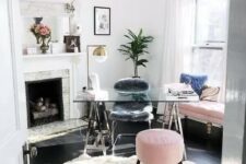 a light-filled home office with a fireplace, a glass trestle desk, a pink sofa and a pouf, potted plants, brass lamps looks cute and cool