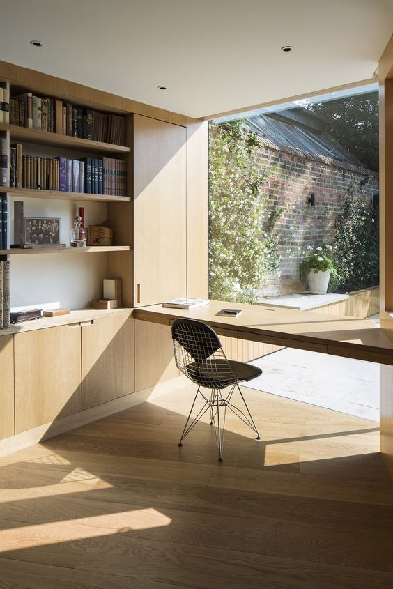 a minimalist home office with a built-in plywood storage unit with open storage compartments, a windowsill desk and a black chair