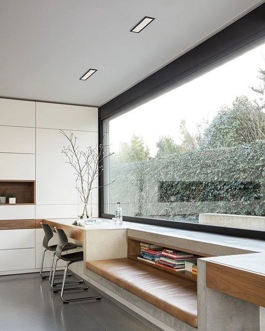 a minimalist home office with a panoramic window, a white sleek storage unit, a windowsill daybed and a built in desk