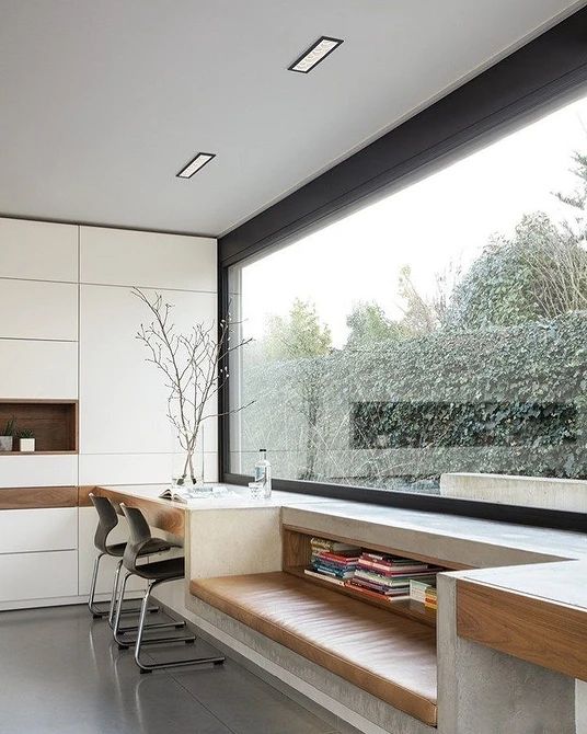 a minimalist home office with a panoramic window, a white sleek storage unit, a windowsill daybed and a built-in desk