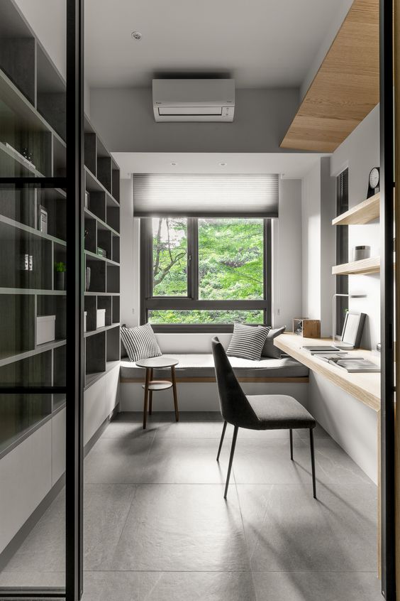 a minimalist home office with a windowsill daybed, a large storage unit, floating shelves and a desk, a grey chair